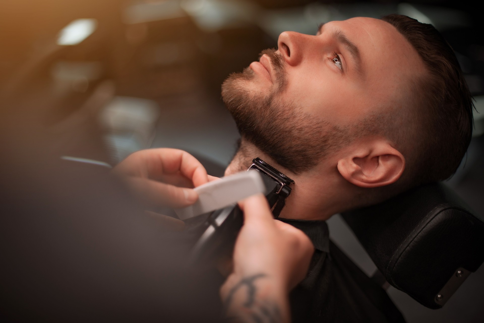 Close-up of a man receiving a precise neck and beard trim with electric clippers at a modern barbershop, showing careful grooming and relaxation in a professional setting.